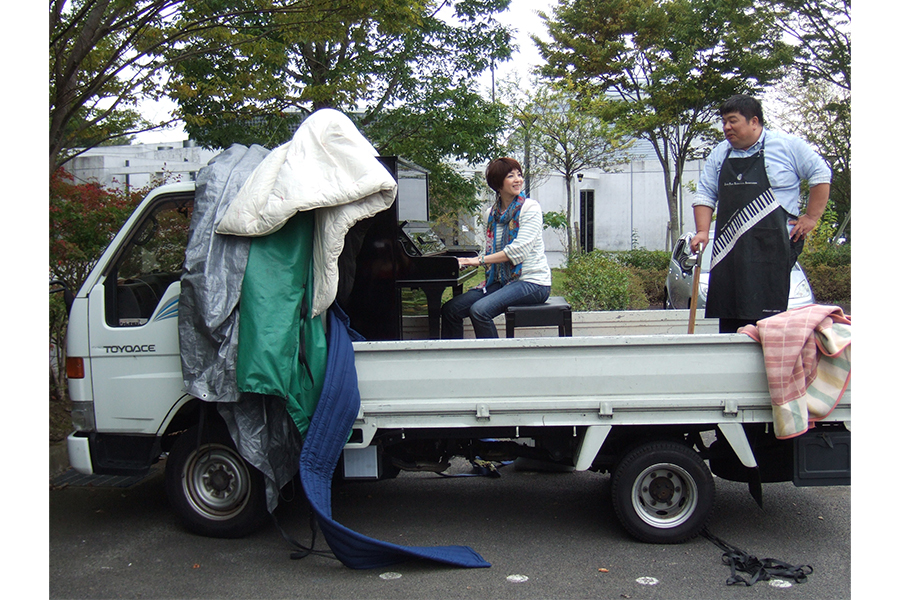 宮城県多賀城市に住む当時音大を目指していた生徒のお宅までピアノを届けに行く前に試奏する西村さんと調律師さん（2011年9月）【写真提供：（株）モデラート】