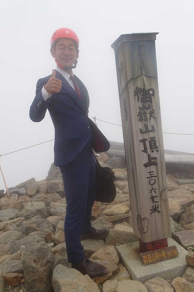 御嶽山山頂でポーズを決める「オーダースーツSADA」の佐田展隆社長